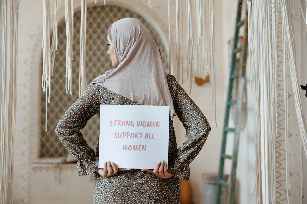 Services A woman in a hijab holds a sign promoting women's solidarity indoors.